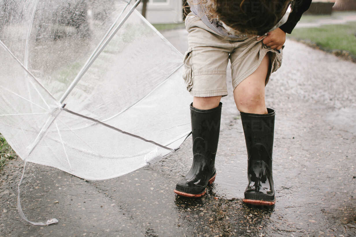 Girl In Rubber Boots Holding Umbrella While Standing On Wet Road