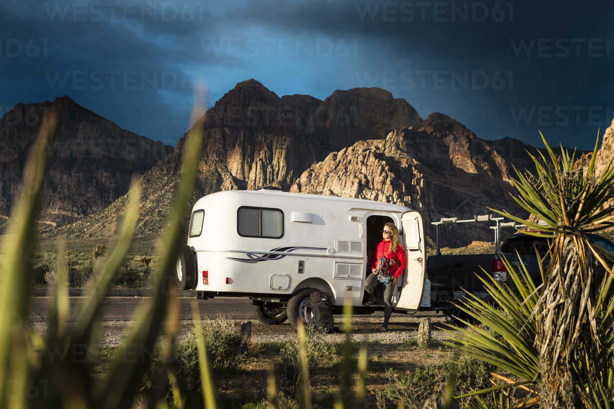 Woman Standing By Camper Trailer Against Mountains And Sky Stockphoto