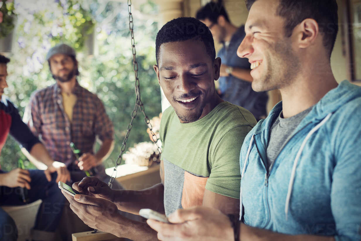 A Group Of Friends Men And Women At A House Party Two Men Looking At Their