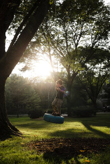 Full Length Of Playful Boy Standing On Tire Swing While Playing At Park During Sunset Stockphoto