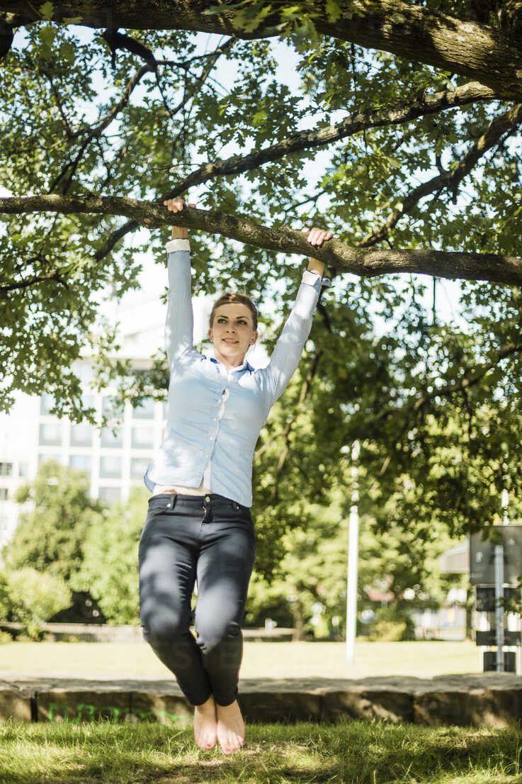 https://images1.westend61.de/0001074203pw/woman-in-urban-park-hanging-at-branch-of-a-tree-MOEF01553.jpg