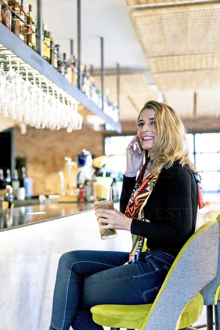 Smiling Woman With Cocktail And Cell Phone Sitting At The Counter Of A Bar Stockphoto