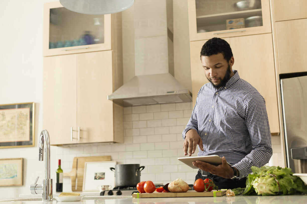 Mixed Race Man Cooking With Tablet Computer In Kitchen Stockphoto