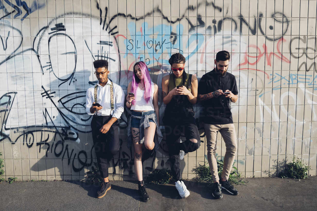 Group Of Friends Using Smartphones At A Graffiti Wall In The City Stockphoto