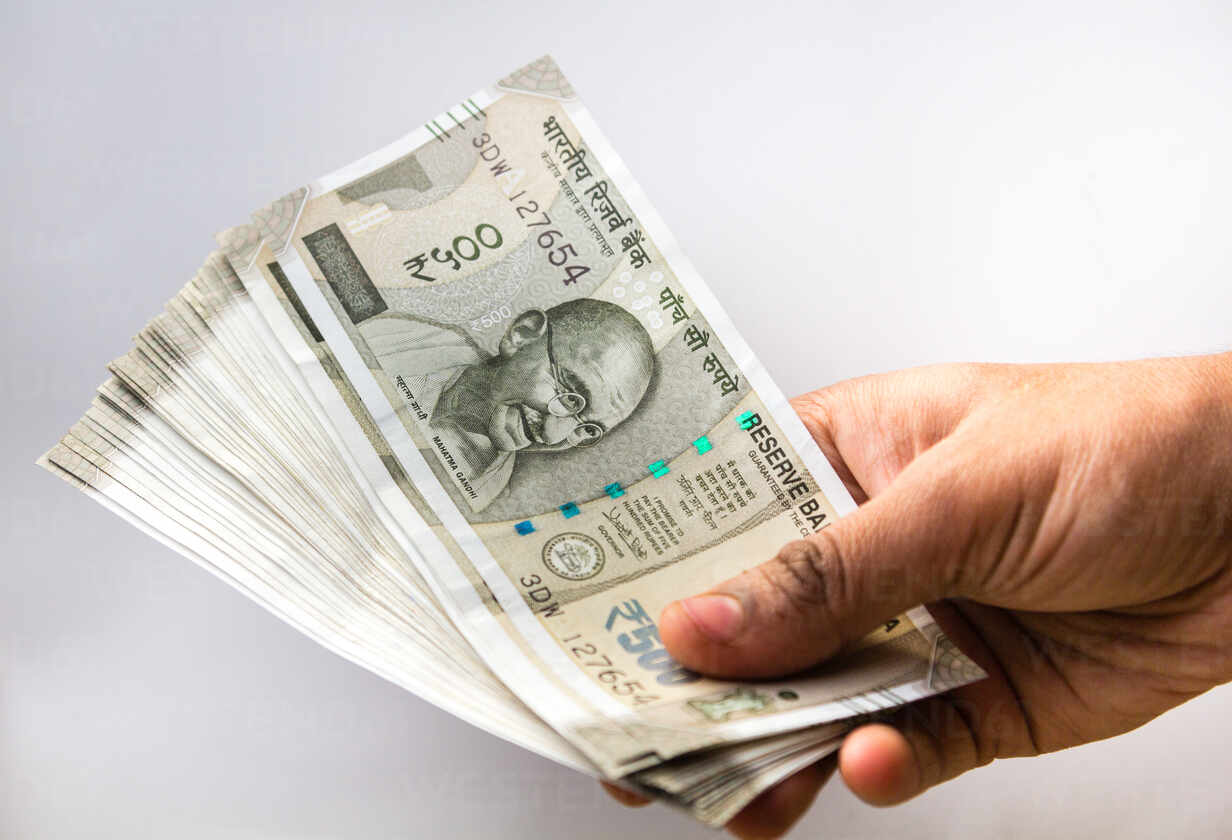 Cropped Hand Holding Indian Currency Against White Background Stockphoto