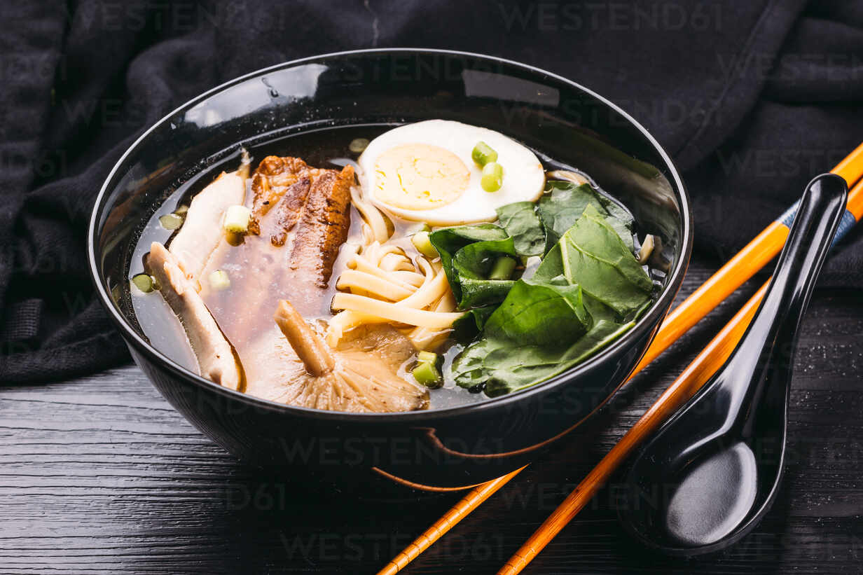 Bamboo Chopsticks And Ceramic Spoon Lying Near Bowl With Delicious Ramen On Black Lumber Tabletop Stockphoto