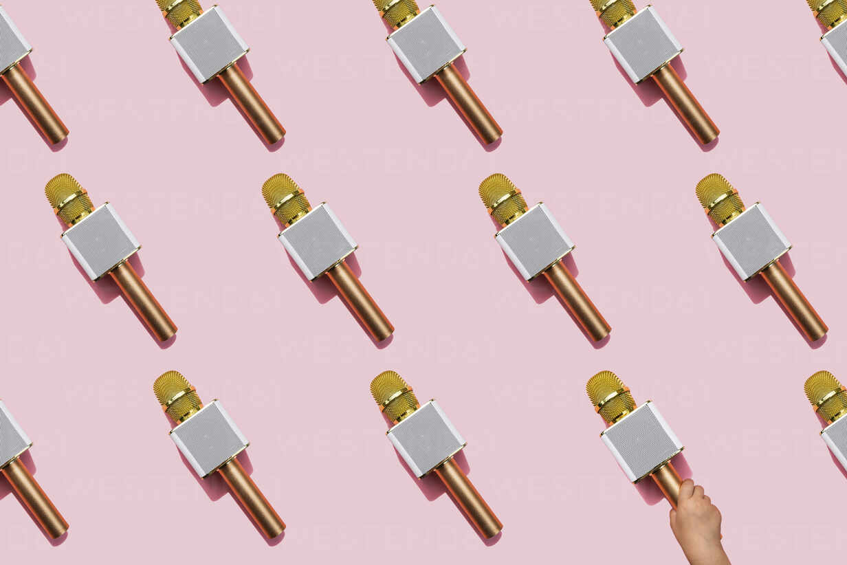 Pattern Of Golden Microphones Against Pink Background With Hand Of Baby Girl Picking One Up Gemf