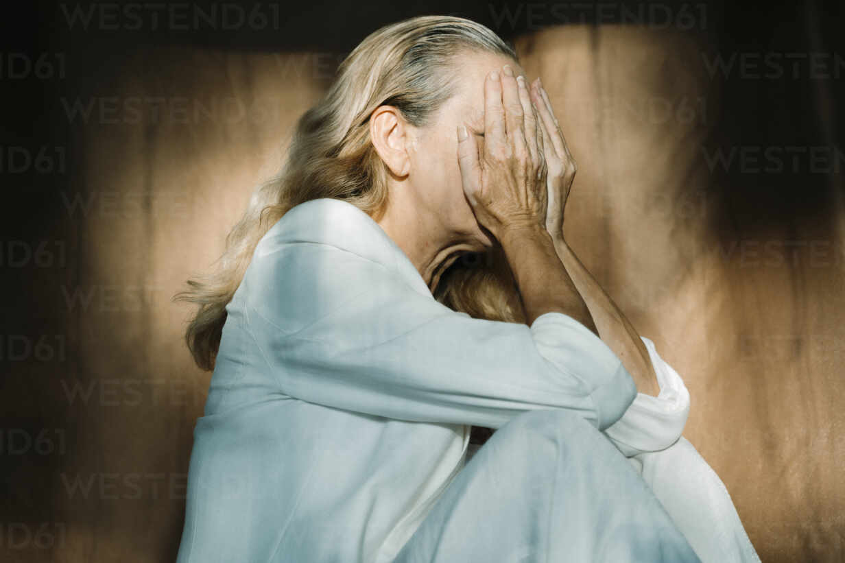 Sad Senior Woman Sitting Alone With Hands Covering Face Stockphoto