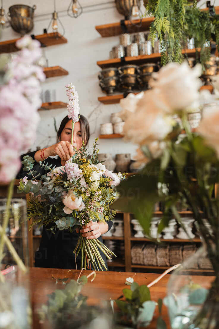 Concentrated Young Female Floristry Designer With Big Bouquet Of Fresh Blooming Flowers And Green Foliage Standing