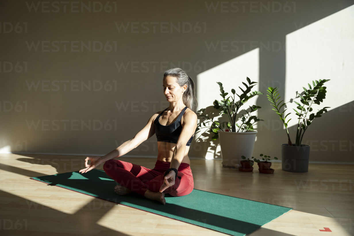 Female Yoga Instructor Meditating On Exercise Mat In Living Room On Sunny Day Mcvf 27exp Westend61