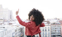 Back View Of African American Female With Curly Hair In Stylish Outfit Standing On Balcony And Looking At City Buildings Stockphoto