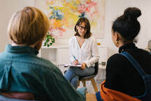 Back View Of Unrecognizable Male In Casual Clothes Wiping Away Tears While Sitting On Chair With Ethnic Wife And Psychologist During Therapy Session Stockphoto