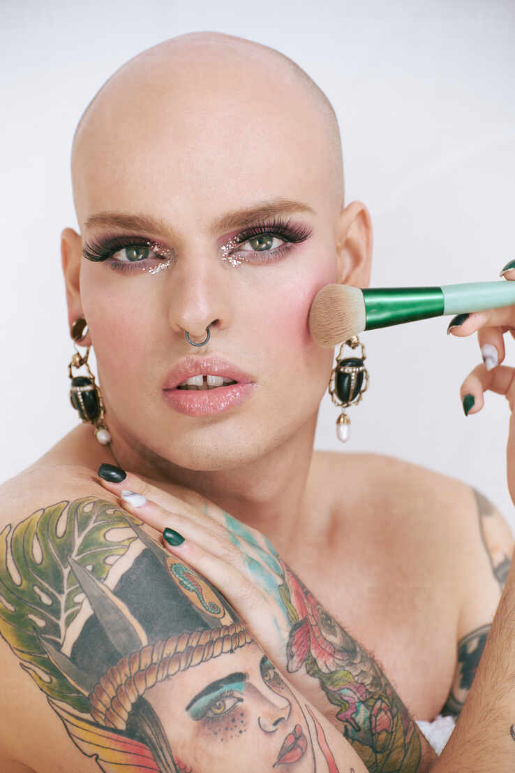 Junger Transgender Mann Mit Langen Wimpern Und Tattoo Halt Kosmetikapplikatoren Wahrend Er In Die Kamera Schaut